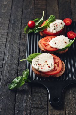 Açık sandviç veya mozzarella peynirli bruschetta, domates ve fesleğen, koyu ahşap arka planda Caprese..