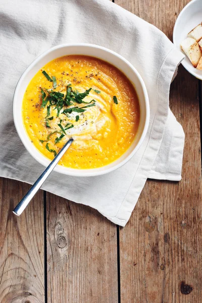 Ahşap bir arka planda otlu balkabağı kremalı çorba..