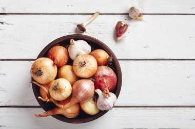 Beyaz ahşap arka planda bir kasede soğan ve sarımsak..