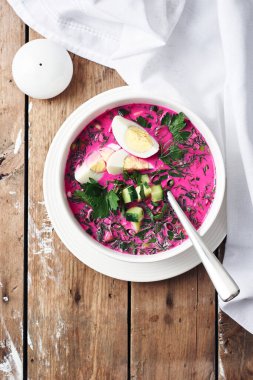 Soğuk pancar çorbası, salatalık, yumurta ve otlar ahşap bir masada..