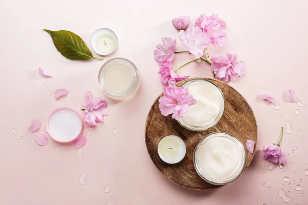 Natural body care cream and pink cherry flowers. Flat lay.