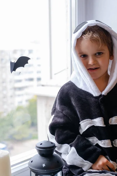 Маленький мальчик в костюме скелета и шляпе ведьмы на Хэллоуин сидит у окна и смеется — стоковое фото