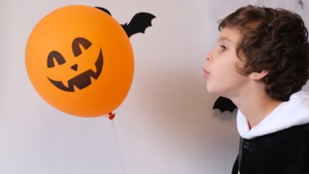 Мальчик в костюме, дующий на оранжевый шар на Хэллоуин, концепция фестиваля Хэллоуина. — стоковое видео