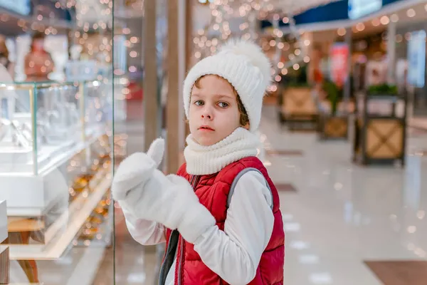 Beyaz tüylü şapkalı çocuklar pencereden bakıyorlar ve markette bir şey gösteriyorlar..