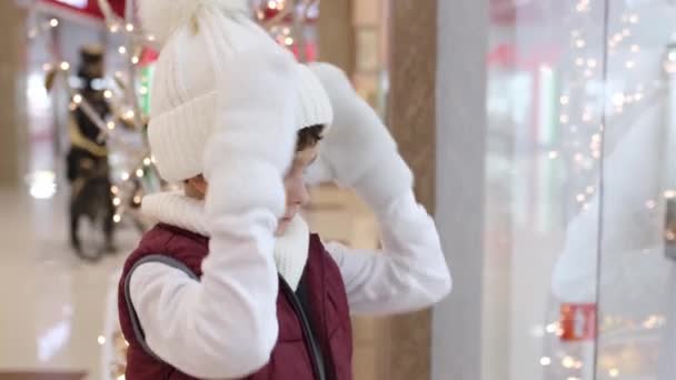 Pojken drar sin vita hatt över ögonen nära fönstret på marknaden. — Stockvideo