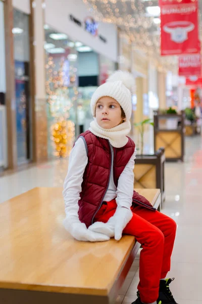 Lindo chico en un sombrero blanco esponjoso en un centro comercial contra el fondo de luces brillantes —  Fotos de Stock