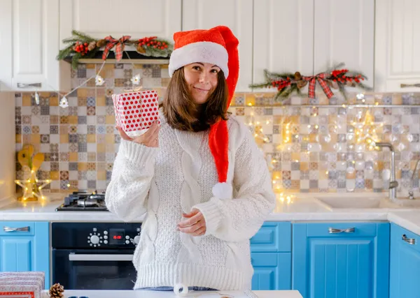 Happy woman in a Santa hat is holding a newly wrapped gift. — Stock Photo, Image