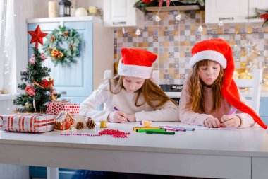 Noel Baba şapkalı çocuklar Noel Baba 'ya Noel süslemeli mutfakta bir mektup yazıyorlar.