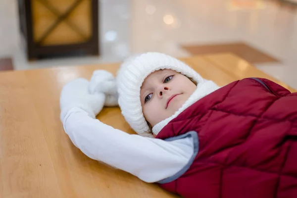 Lindo chico en un sombrero blanco esponjoso en un centro comercial contra el fondo de luces brillantes —  Fotos de Stock