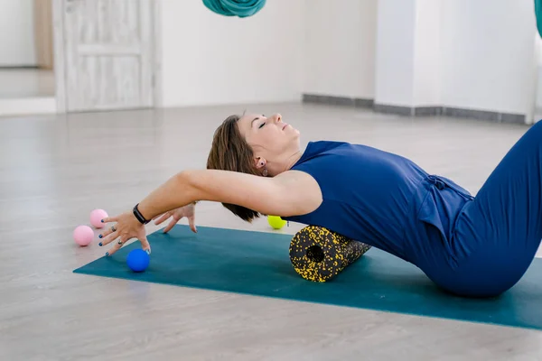 Brunnet Woman lie on yogi mat use Myofascial release massage roll on back