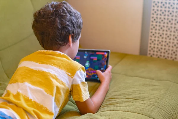 Мальчик в желтой и белой футболках с энтузиазмом играет в игру на планшете — стоковое фото