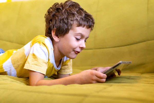 Chico en amarillo y blanco camiseta con entusiasmo juega un juego en una tableta —  Fotos de Stock