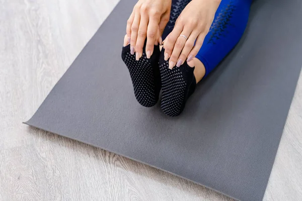 Vista dall'alto a mani che tengono il piede di una femmina seduta su un tappetino di yoga all'aperto su un pavimento di legno Foto Stock