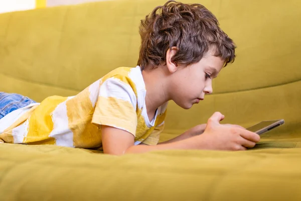 Chico en amarillo y blanco camiseta con entusiasmo juega un juego en una tableta —  Fotos de Stock