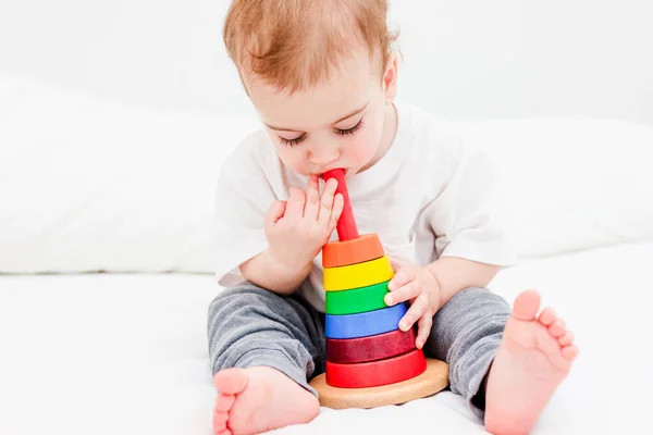 Прелестный ребенок 1 год в белой футболке, играющий с деревянной пирамидой. Концепция деревянной игрушки, развитие детей — стоковое фото