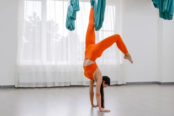 Брюнетка женщина 25 лет висит вверх ногами, используя гамак для йоги. Леди в белом и фиолетовом спортивном костюме — стоковое фото