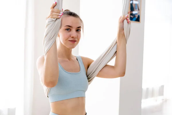 Wanita 25 tahun tergantung menggunakan tempat tidur gantung untuk yoga. Wanita mengenakan pakaian olahraga biru muda — Stok Foto