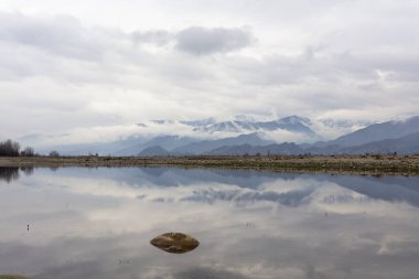 Karla kaplı dağlarda deniz veya göl suyunda yansımalar var.