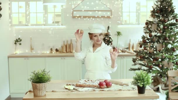 Um chef alegre prepara um bolo de Natal. Senhora cozinhe em um avental bonito quebrando um ovo em farinha para fazer bolo. O processo de cozinhar. Passo a passo. Atmosfera insuperável pré-férias e conforto doméstico — Vídeo de Stock