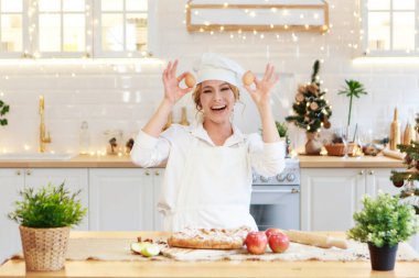 Neşeli bir şef Noel pastası hazırlar. Bayan önlüklü aşçı kek yapmak için una yumurta kırıyor. Yemek pişirme süreci. Adım adım. Eşsiz tatil öncesi atmosfer ve ev konforu