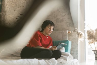 Evde çalışmak: yatakta dizüstü bilgisayarı olan bir kız. İş kadını. Uzaktan çalışma. Kanepede alışveriş yap. İnternet üzerinden alışveriş