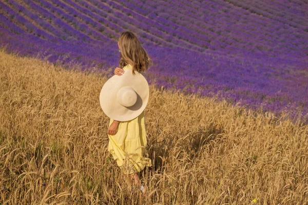 Ontmoeting van twee werelden: een meisje in een gele jurk tussen een tarwe- en lavendelveld — Stockfoto