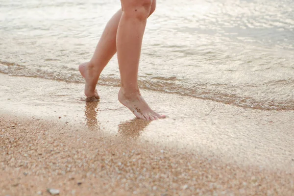 Gebräunte Beine im Sand in Großaufnahme. eine Welle rollt auf den Sand. Sommerurlaub am Meer — Stockfoto