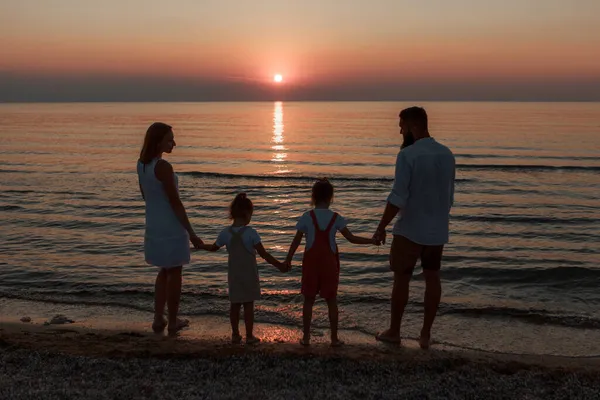 Grande famille sur la plage. Des silhouettes de gens contre le coucher du soleil. 4 personnes se tenant la main — Photo