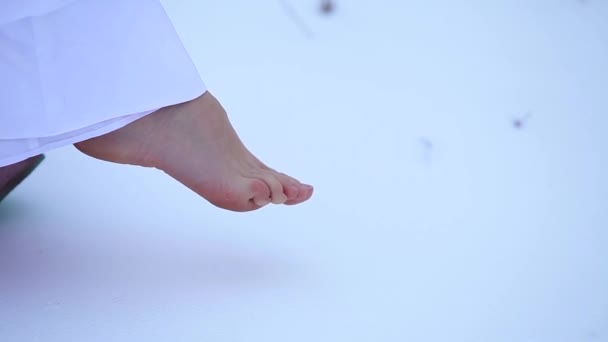 Pie desnudo en el primer plano de la nieve. El dobladillo de un vestido blanco en la nieve. congelación de las extremidades — Vídeos de Stock