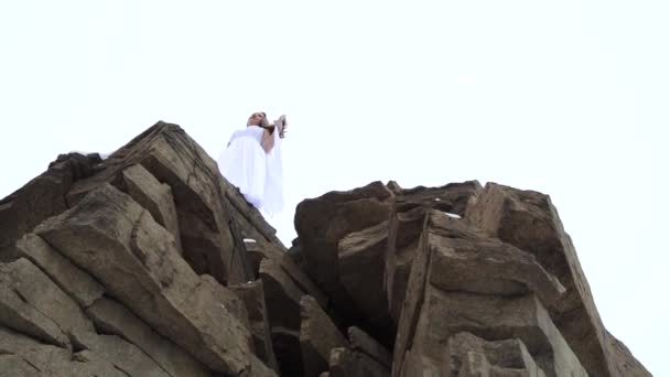Vue du bas : la mariée sur le bord de la falaise. Séance photo extrême : une fille en robe blanche en hiver — Video
