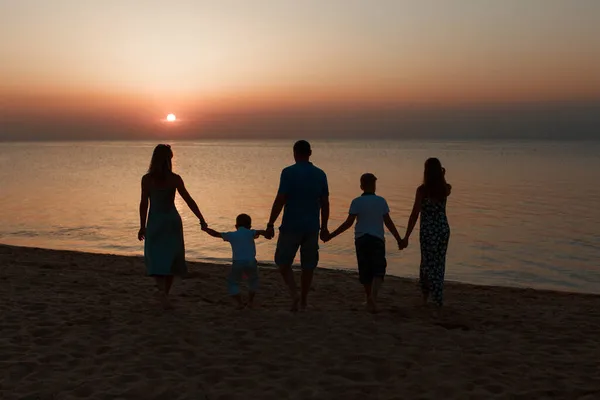 Sahilde büyük bir aile. Gün batımına karşı insanların siluetleri. El ele tutuşan 5 kişi — Stok fotoğraf