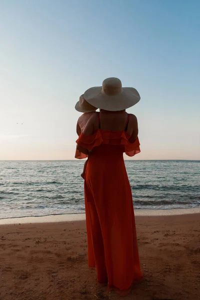 Utazás a tengerhez. Egy lány egy ruhában és kalapban sétál a parton. Egy turista sétál a tengerparton. forró kirándulások az ünnepi időszakban. másolás helye — Stock Fotó