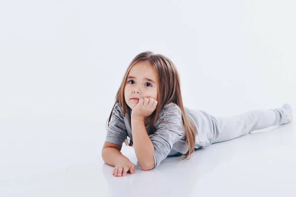 Uma menina deitada no chão sobre um fundo branco. Criança promove roupas infantis — Fotografia de Stock