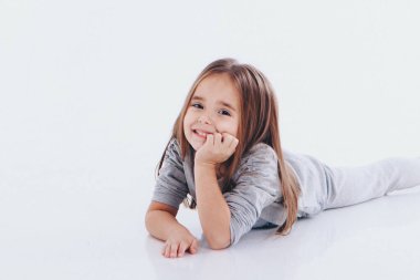 Beyaz bir arka planda yerde yatan küçük bir kız. Çocuk, çocuk kıyafetlerinin reklamını yapıyor.