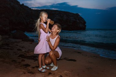 Diyet olsun. Sağlıklı beslenme ve dinlenme. Kadın ve kız cam arka planda temiz su içerler. Kumsalda bir kadın hayatın tadını çıkarır.