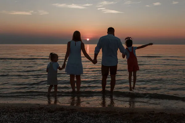 Grande família na praia. Silhuetas de pessoas contra o pôr-do-sol. 4 pessoas de mãos dadas — Fotografia de Stock