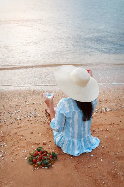 Fogyókúra. Egészséges evés és pihenés. nő iszik tiszta vizet üveg háttér tenger és eszik epret. Egy nő a parton élvezi az életet. — Stock Fotó