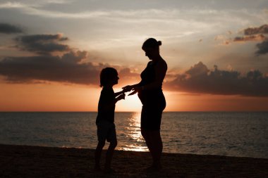 Sahilde bir aile. Gün batımına karşı insanların siluetleri. İki kişi el ele tutuşuyor.