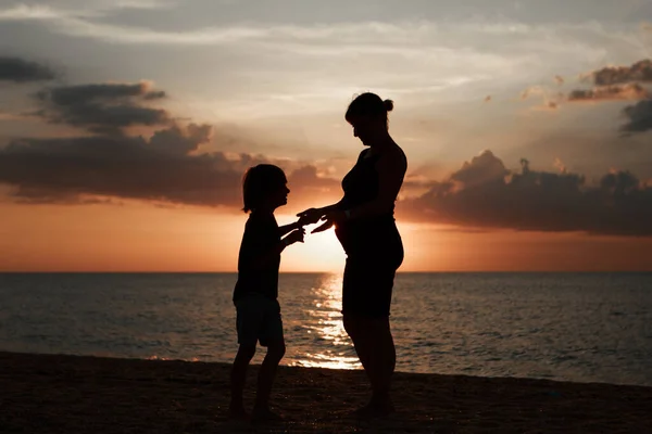 Rodina na pláži. Siluety lidí proti západu slunce. 2 lidé se drží za ruce — Stock fotografie