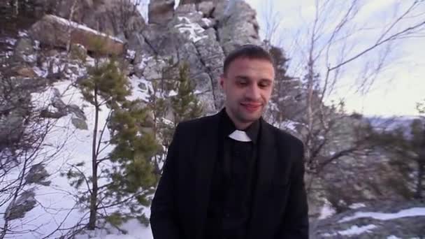 Kněz káže na hoře. Muž v šatech pastora stojí na kameni. Zima a zima v horách — Stock video