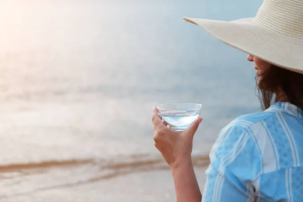 Kosthold. Sunn mat og hvile. kvinne drikker rent vann i glassbakgrunn sjø. En kvinne på stranden nyter livet. – stockfoto