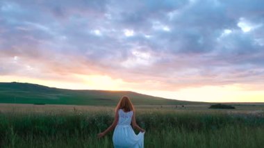 Buğday tarlasında duran genç bir kadın ve arka planda gün doğumu