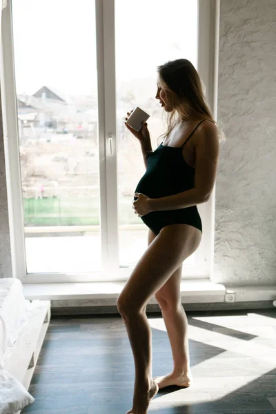 Retrato de una mujer embarazada con una taza en la mano en la ventana. Calma futura madre. Descanso para el almuerzo o el café, té —  Fotos de Stock