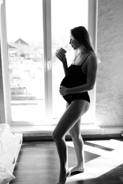 Pencerede elinde bir Fincan ile hamile bir kadının portresi. Sakin müstakbel anne. Öğle yemeği veya kahve, çay için mola — Stok fotoğraf