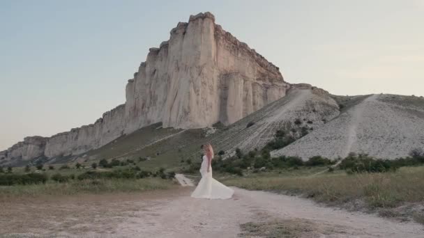 Young beautiful blonde woman in a white dress spinning in the mountain. Attractive fashion model with flying hair. Beautiful girl woman shakes hair. Slow motion — Stock Video