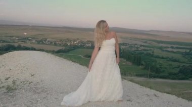 Dağda dönen beyaz elbiseli güzel sarışın kadın. Uçan saçlı çekici bir manken. Güzel kız saçlarını sallıyor. Yavaş çekim