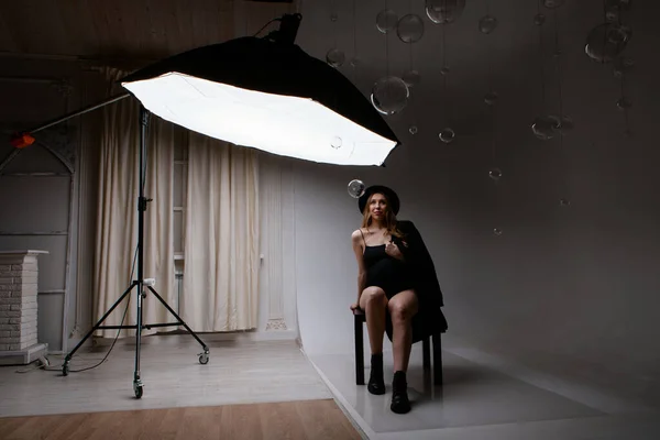 Une femme enceinte en costume noir caresse son ventre sur un fond blanc. Une fille dans le studio sous les projecteurs. éclairage professionnel. — Photo