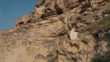 Dağda dönen beyaz elbiseli güzel sarışın kadın. Uçan saçlı çekici bir manken. Güzel kız saçlarını sallıyor. Yavaş çekim