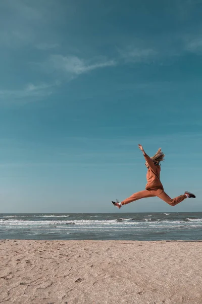 Kvinne som hopper lykkelig på stranden med en blå himmel og hav i bakgrunnen – stockfoto