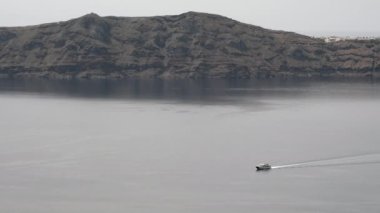 Küçük bir feribot Santorini limanına yaklaşıyor ve Nea Kameni volkanının yanından geçiyor.